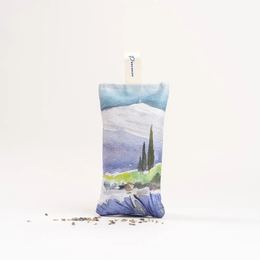 The L&#39;AUGUSTE PROVENCE - FRENCH LAVENDER SACHET FROM PROVENCE is a small handcrafted pouch with a countryside watercolor design, upright shape, &quot;L&#39;AUGUSTE PROVENCE&quot; tag, and dried lavender pieces at its base.