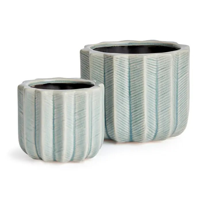 The NAPA HOME AND GARDEN - VELA POT, LARGE by NAPA HOME AND GARDEN features a fully visible ceramic planter with a light blue chevron pattern and textured vertical ridges, forming part of a charming decorative set. A smaller matching pot is partially displayed in the foreground on the left.