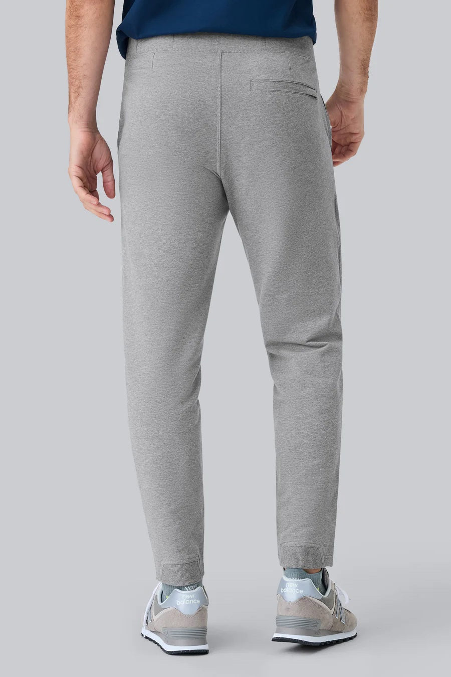 A person wearing MACK WELDON ACE Sweatpants in Ice Storm Heather, a dark blue shirt, and gray sneakers with white soles stands on a light gray background, shown from the side with one arm relaxed.