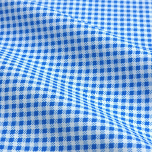 A man with short dark hair and a trimmed beard, wearing the COLLARS AND CO - Oxford Button Down Collar Apex Performance Dress Shirt in Micro Blue Gingham, holds open a glass door and looks left in a bright, modern space.