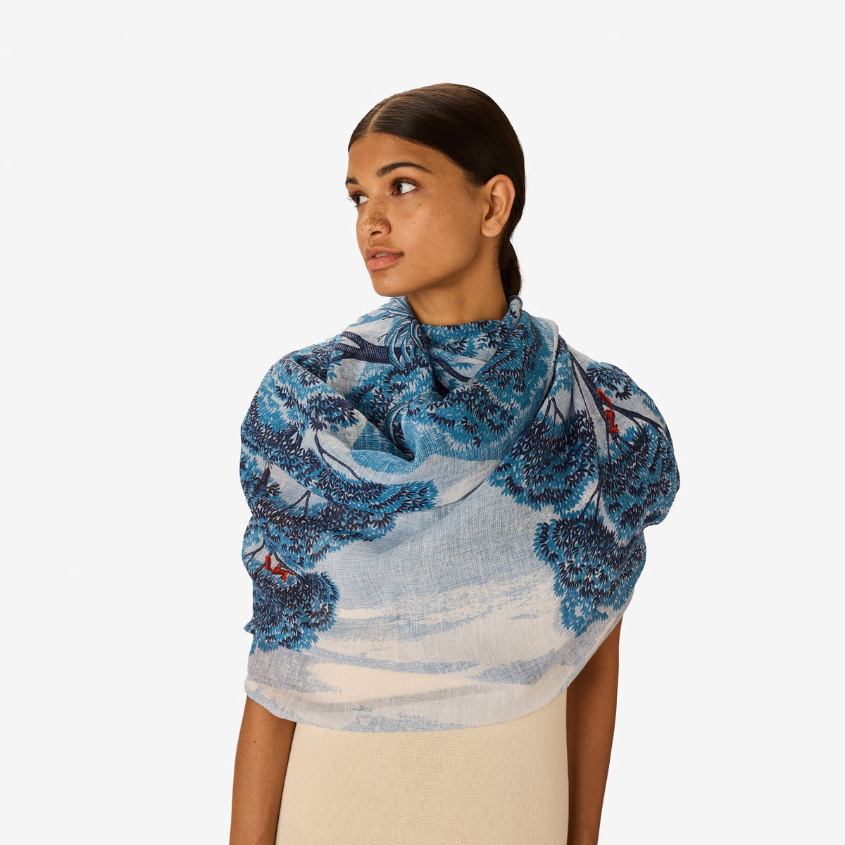 The INOUI EDITIONS AMBROISE SCARF IN DUCK BLUE by INOUI features an artistic blue and orange tree print on a light blue and white background, reminiscent of hand-printed linen cotton scarf blends.