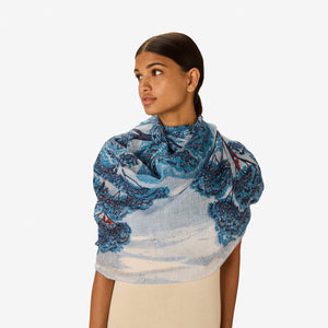 The INOUI EDITIONS AMBROISE SCARF IN DUCK BLUE by INOUI features an artistic blue and orange tree print on a light blue and white background, reminiscent of hand-printed linen cotton scarf blends.
