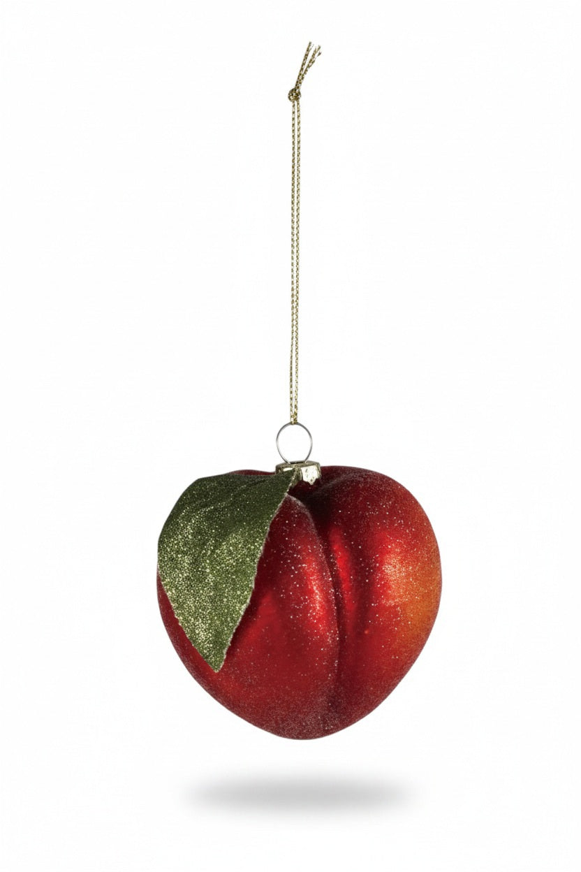 A green tin filled with paper shreds, a citrus slice ornament, a small round ornament, and a PEACH ORNAMENT WITH GLITTER.