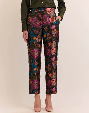 A person wears the HINSON WU Jolene Jacquard Pant in Floral Bouquet—high-waisted, ankle-length tailored trousers featuring a vibrant floral pattern in pink, purple, blue, and orange—paired with a dark green shirt and light pink heels.