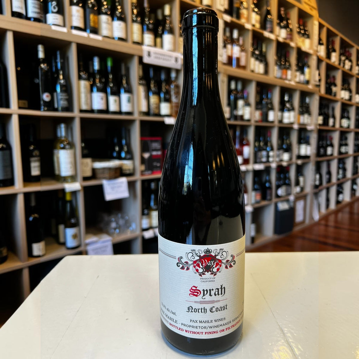 A bottle of PAX ‘NORTH COAST’ SYRAH 2023 from WINE: KELLOGG SELECTIONS, featuring a cream label with red and black text and a decorative crest, stands against a plain white background—an elegant tribute to cool-climate Syrah crafted in the spirit of esteemed winemakers such as Pax Mahle.