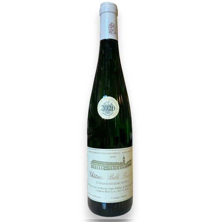A green glass bottle of CHÂTEAU BELÁ RIESLING 2020 by WINE: KELLOGG SELECTIONS stands on a white counter in a wine shop, with blurred shelves behind it, highlighting the elegance of this Slovakian riesling from near the Danube.