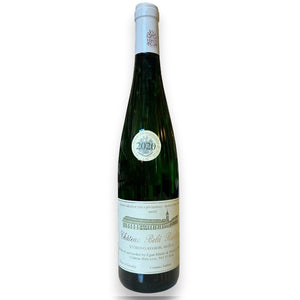 A green glass bottle of CHÂTEAU BELÁ RIESLING 2020 by WINE: KELLOGG SELECTIONS stands on a white counter in a wine shop, with blurred shelves behind it, highlighting the elegance of this Slovakian riesling from near the Danube.