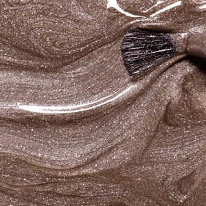 A close-up of a brush spreading MANUCURIST - GREEN™ NAIL POLISH IN QUARTZ by MANUCURIST INC, showcasing its shimmery, metallic brown vegan formula with visible sparkles and swirling patterns.