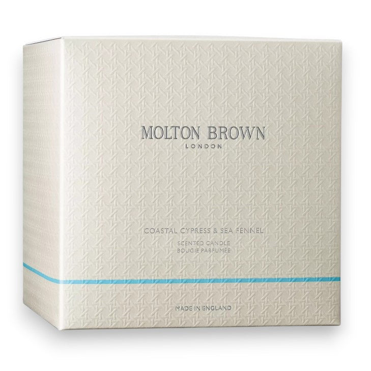 A dark glass MOLTON BROWN - COASTAL CYPRESS 1 WICK CANDLE, labeled &quot;Molton Brown London&quot; with &quot;Coastal Cypress &amp; Sea Fennel&quot; beneath, photographed on a white background, evokes marine notes and the freshness of sea fennel.