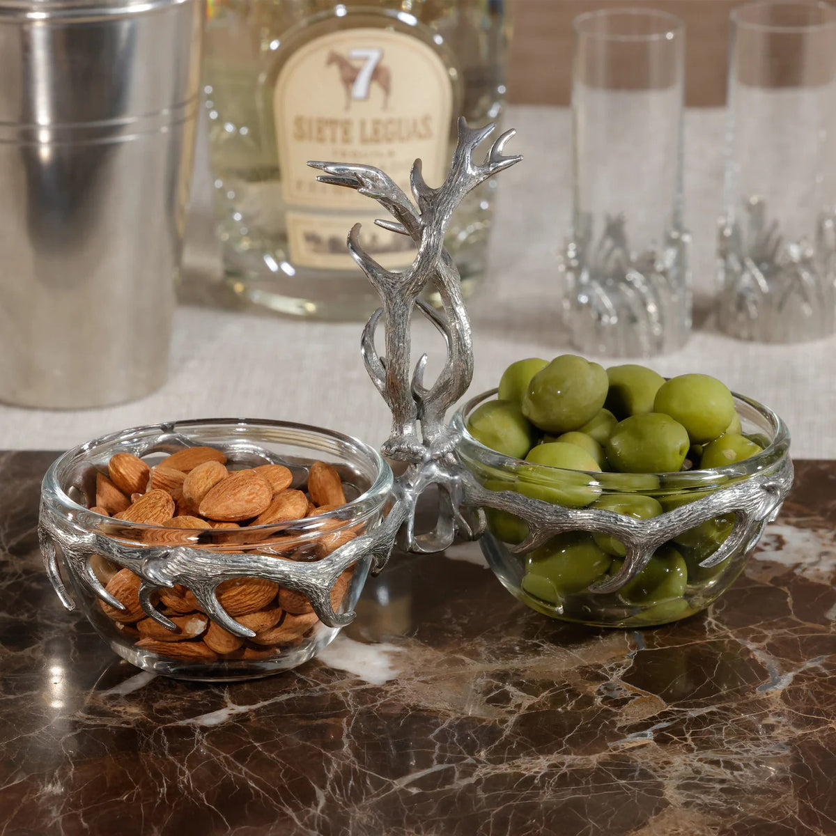 The ZODAX ST. ANTON Pewter and Glass Condiment Set features two clear glass bowls joined by a pewter antler-shaped holder with a central handle. Size: 3.5 in x 7.75 in x 5.25 in.