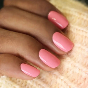 A hand with short, neatly manicured nails painted with MANUCURIST - GREEN™ Nail Polish in Pink Paradise by MANUCURIST INC rests on a cream-colored knitted fabric.