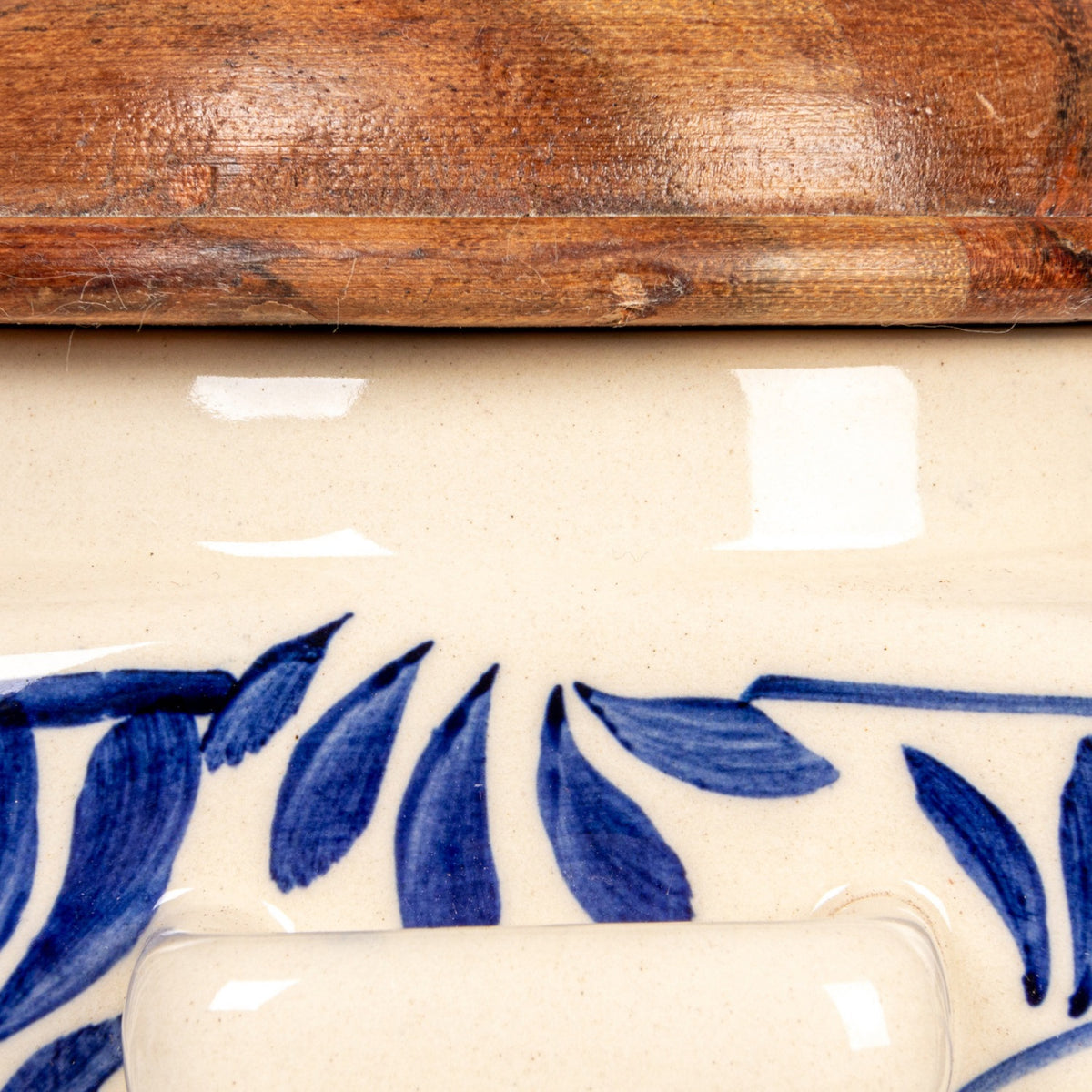 The HAND-PAINTED STONEWARE CANISTER WITH LID AND SPOON by CREATIVE COOP features blue floral designs, an acacia wood lid, and a wooden spoon in a side holder—perfect as farmhouse kitchen decor. Sits on a white background.