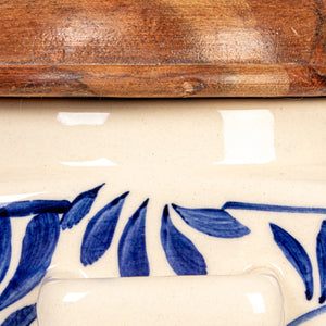 The HAND-PAINTED STONEWARE CANISTER WITH LID AND SPOON by CREATIVE COOP features blue floral designs, an acacia wood lid, and a wooden spoon in a side holder—perfect as farmhouse kitchen decor. Sits on a white background.