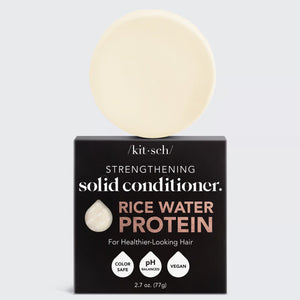 A round, off-white solid conditioner bar rests on its black and white packaging labeled "KITSCH - RICE WATER PROTEIN CONDITIONER BAR FOR HAIR GROWTH," promoting benefits for damaged hair repair. The product is color safe, pH balanced, and vegan.