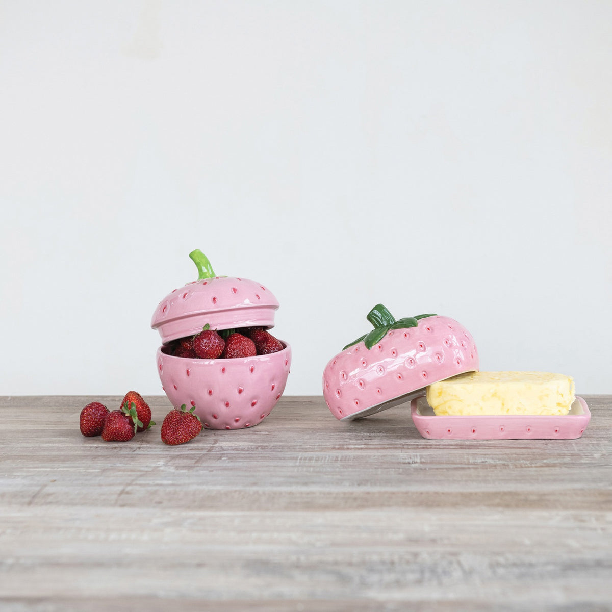 The CREATIVE COOP HAND-PAINTED CERAMIC STRAWBERRY SHAPED JAR WITH LID is a pink, strawberry-inspired storage container with a green stem handle—ideal for adding decorative charm to your kitchen.