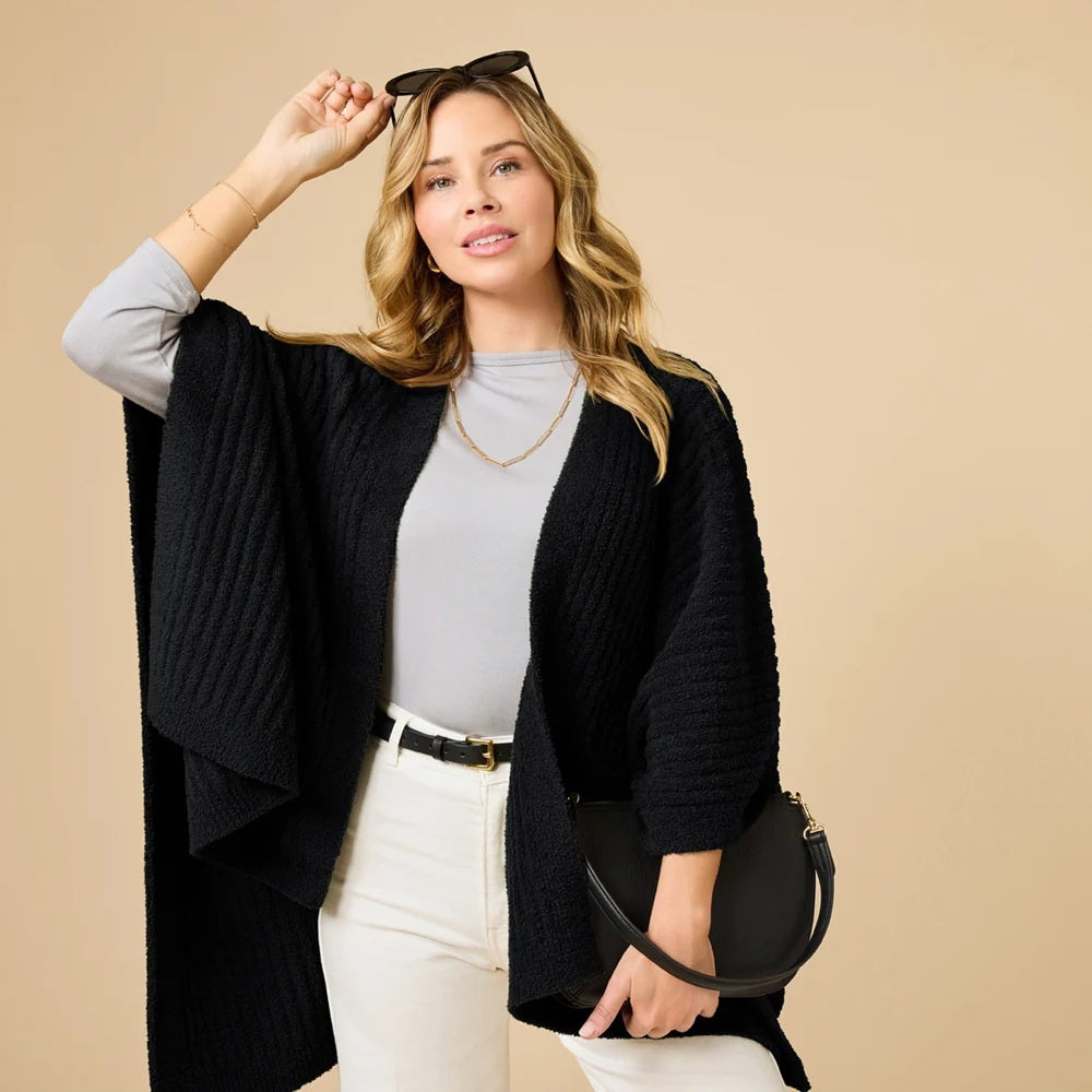 A woman wearing a black SOFTIES - SOLID RIB MARSHMALLOW SHAWL over a grey top and white trousers.