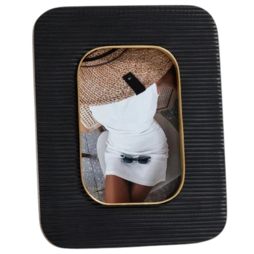 The ZODAX Black Resin Ribbed Photo Frame with Brass Accent (4x6) is shown from the back, featuring a rectangular support stand and two metal clasps securing the rear panel.