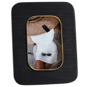 The ZODAX Black Resin Ribbed Photo Frame with Brass Accent (4x6) is shown from the back, featuring a rectangular support stand and two metal clasps securing the rear panel.