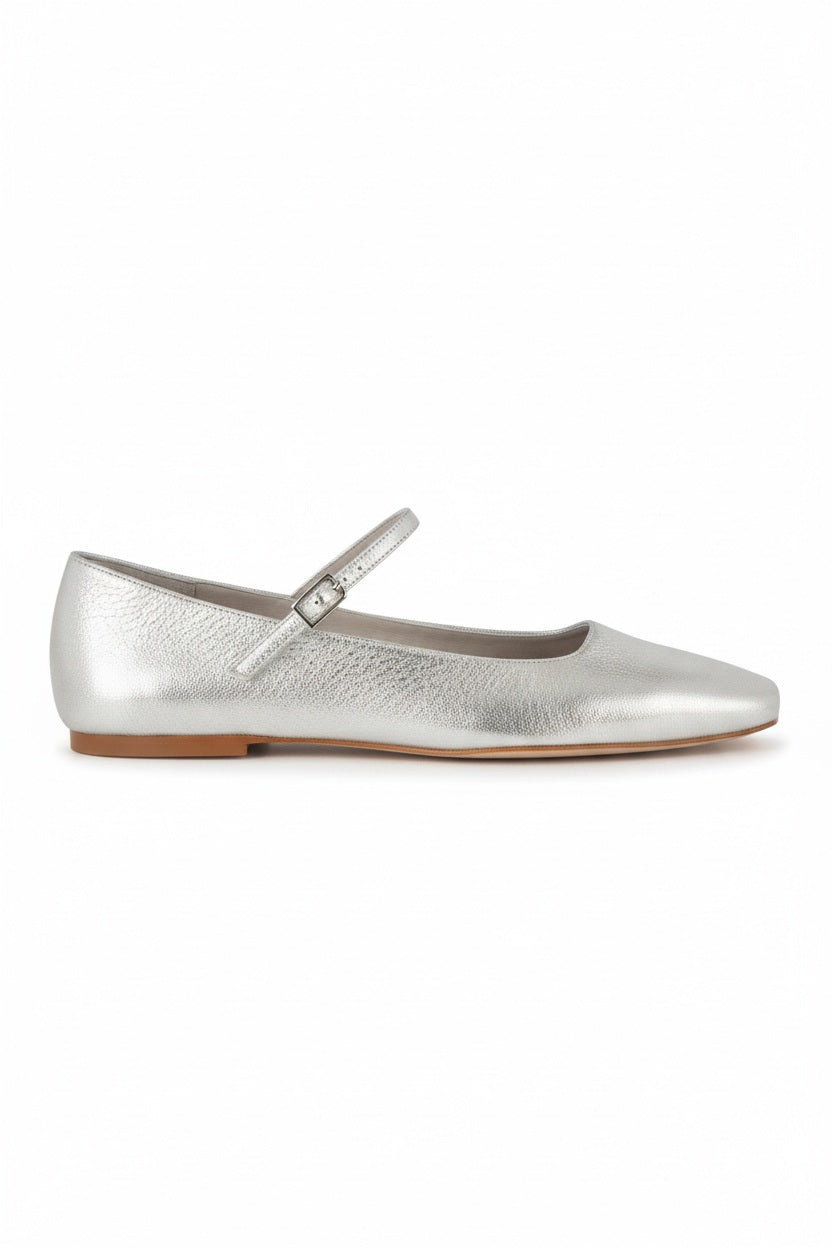 The AUGUSTA - JULIETA MARY JANE by AUGUSTA is a black leather Mary Jane flat with a thin strap and buckle, light brown sole, and subtle square toe, handcrafted in Spain and shown on a light gray background.