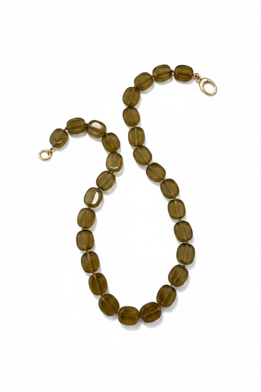 The SANDRINE FRANCE STUDIO - STEFANIE NECKLACE IN BROWN GOLD by SANDRINE FRANCE STUDIO is a hand-knotted piece featuring oval, translucent brown-gold glass beads with gold clasps, arranged in an S-shape on a white background and handcrafted in NYC.