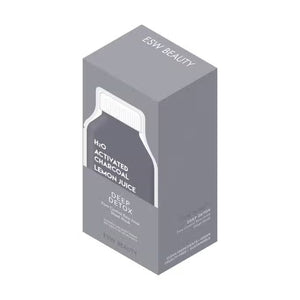 A bottle of ESW BEAUTY - H2O Charcoal Lemon Juice Mask sits on a white surface with lemon halves, a whole lemon, a bowl of white powder, a wooden spoon, and ESW Beauty’s black charcoal powder.