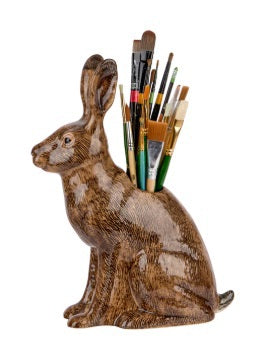 The QUAIL CERAMICS - HARE VASE, LARGE by QUAIL DESIGNS is a hand-painted brown ceramic vase shaped like a hare, displayed with yellow and white flowers and greenery. A single yellow flower lies beside it on a white background.