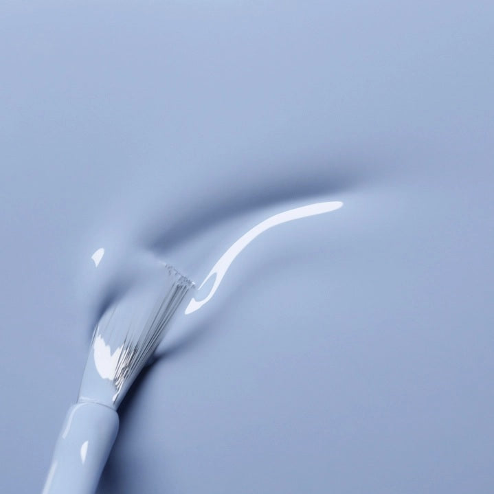 A white nail polish brush spreads MANUCURIST - GREEN™ NAIL POLISH IN LILAS by MANUCURIST INC, a pale lavender vegan formula, smoothly across the surface to create a glossy, even layer.