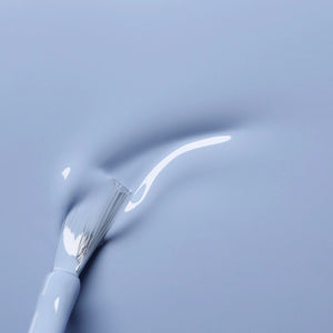 A white nail polish brush spreads MANUCURIST - GREEN™ NAIL POLISH IN LILAS by MANUCURIST INC, a pale lavender vegan formula, smoothly across the surface to create a glossy, even layer.