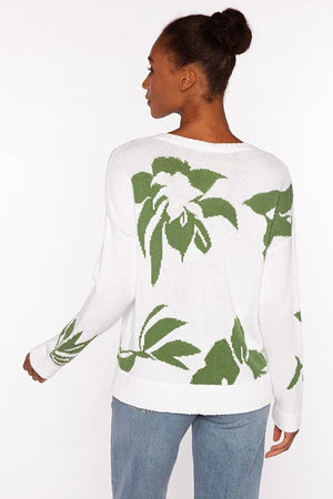 A woman faces forward wearing the KINROSS CASHMERE Intarsia Easy Vee Neck Cotton Sweater, featuring green leaf patterns. Her hair is up, and she pairs it with light blue jeans against a plain white background. 100% cotton by KINROSS.