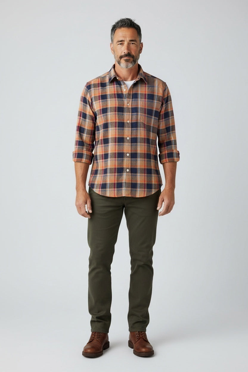 A man stands facing forward, wearing the FRANK &amp; EILEEN Finbar Men’s Button Up in Italian Flannel Orange Plaid, paired with olive green pants and brown shoes against a plain light background.