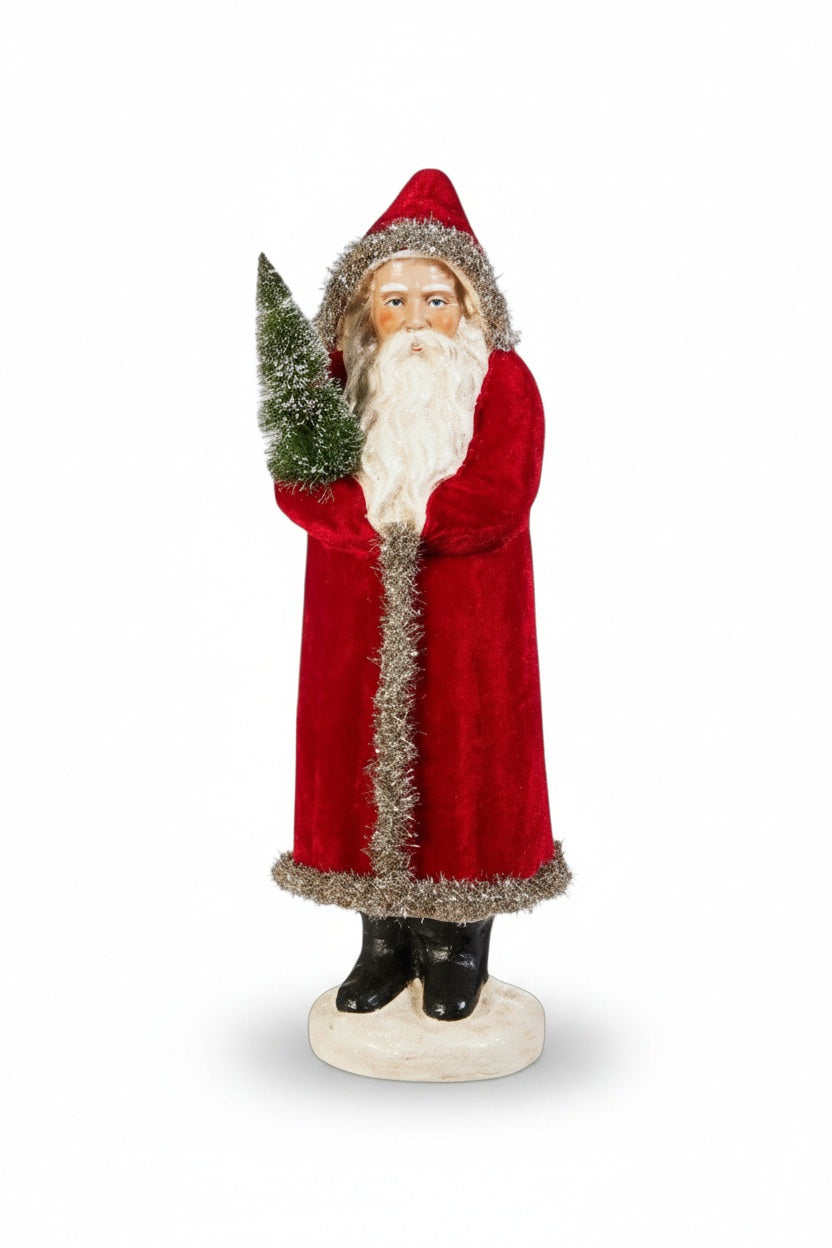 The RED VELVET OLD WORLD SANTA 17" by RAZ IMPORTS features a vintage-style Santa in a long red coat with silver trim, holding a green Christmas tree on a white base—a charming, sustainable addition to festive decor.