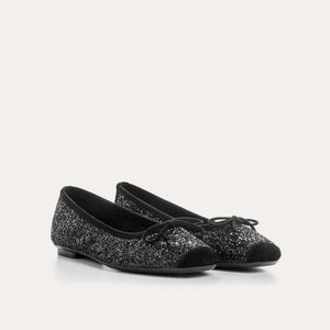 The REQINS Harmony Sequin Ballerina Flats in Noir feature black sequins, black toe caps, and small bows—bringing a touch of everyday luxury against a plain light background.