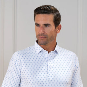 The COLLARS AND CO FEATHERWEIGHT FLEX POLO IN ORACLE WHITE features white fabric with a repeating pattern of small blue 3x3 dot squares. Slightly creased at the center, its 6-way stretch design ensures all-day comfort.