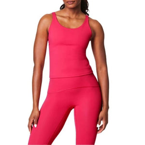 A woman wears the SPANX POWER BOOST SHELF TANK in bright pink with matching leggings, standing with her arms relaxed at her sides against a white background.