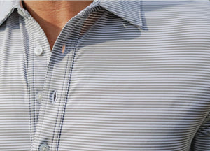 A smiling man with short hair and a beard wears the CRIQUET - Performance Sport Range Polo in Hobby Stripe - Gray as he holds a canned drink in a green koozie, facing slightly to the left against a plain white background.