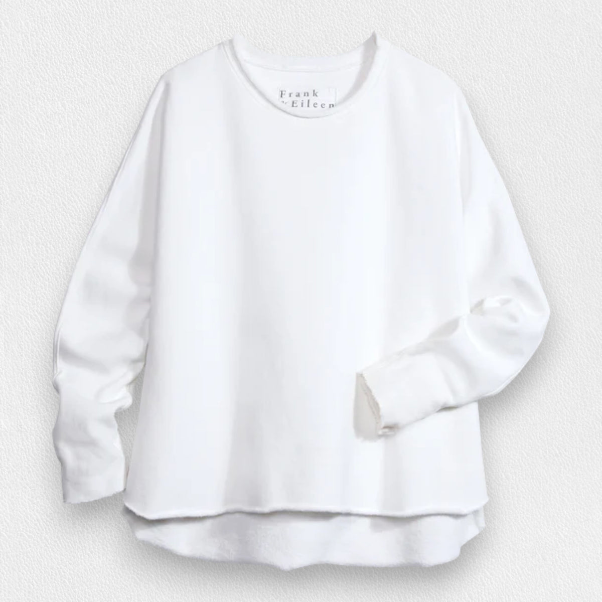 A person with long, wavy blonde hair is standing outdoors near a large tree, wearing the FRANK &amp; EILEEN ANNA LONG-SLEEVE CAPELET in navy over a white shirt and blue pants. The background showcases green foliage and a stone path. The person is smiling and gazing to the side.