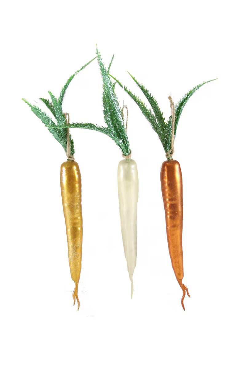 A set of three CARROT ORNAMENTS by CODY FOSTER, featuring decorative pieces in gold, white, and orange glass with green faux leaves on top and varying heights, all displayed against a plain white background.