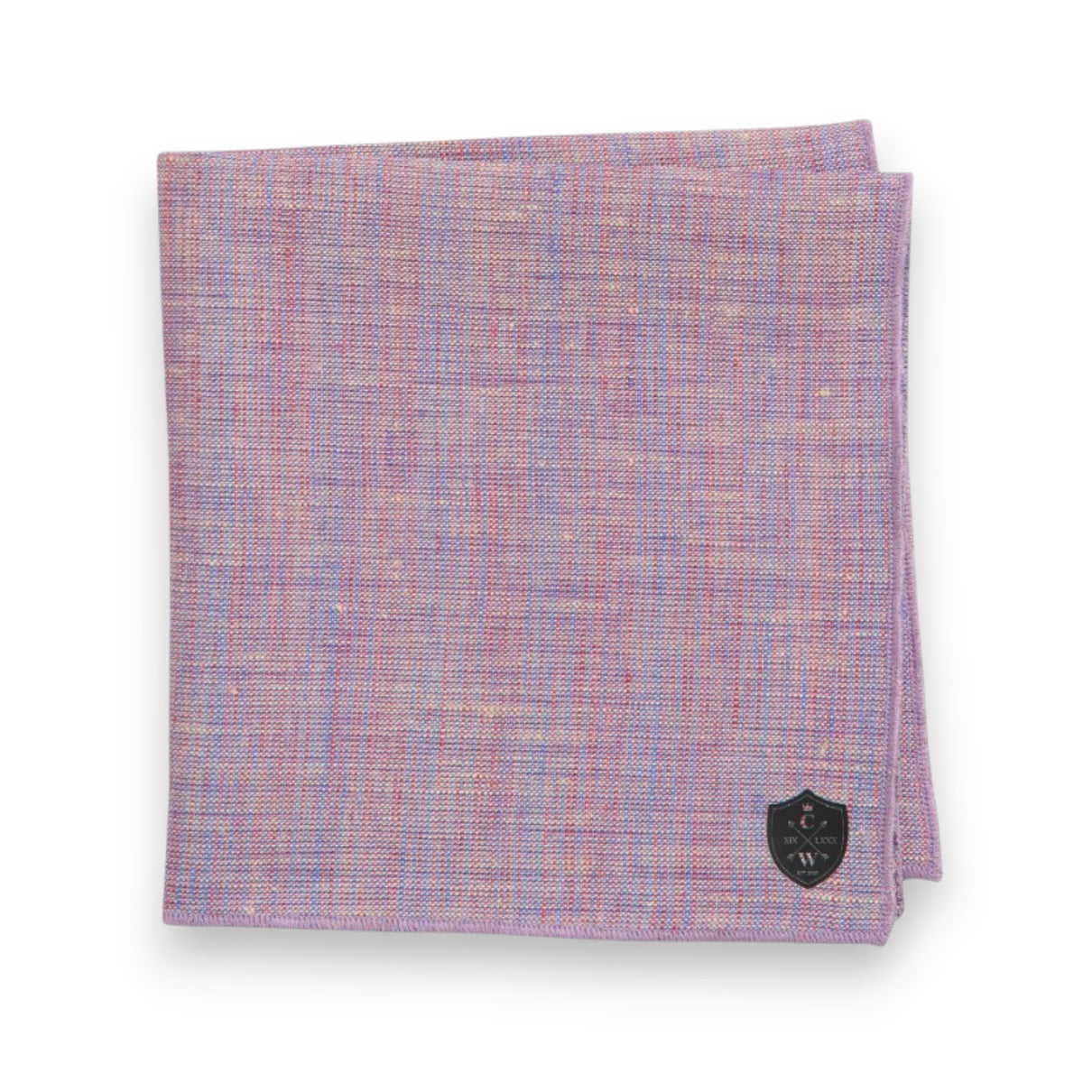 A neatly folded CLIFTON WILSON - LAVENDER BLUE LINEN POCKET SQUARE with a textured design in purple and pink, accented by a small black shield patch with white lettering in the corner, set against a plain white background.