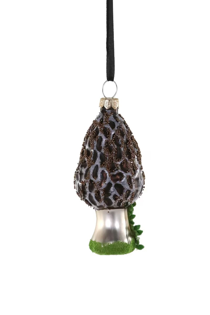 Introducing the MOREL MUSHROOM ORNAMENT by CODY FOSTER, a charming glass Christmas decoration shaped like a mushroom. It features a textured dark brown cap and silver stem, with a small green accent at the base. This delicate ornament hangs elegantly from a black ribbon, making it perfectly sized to complement any festive display.