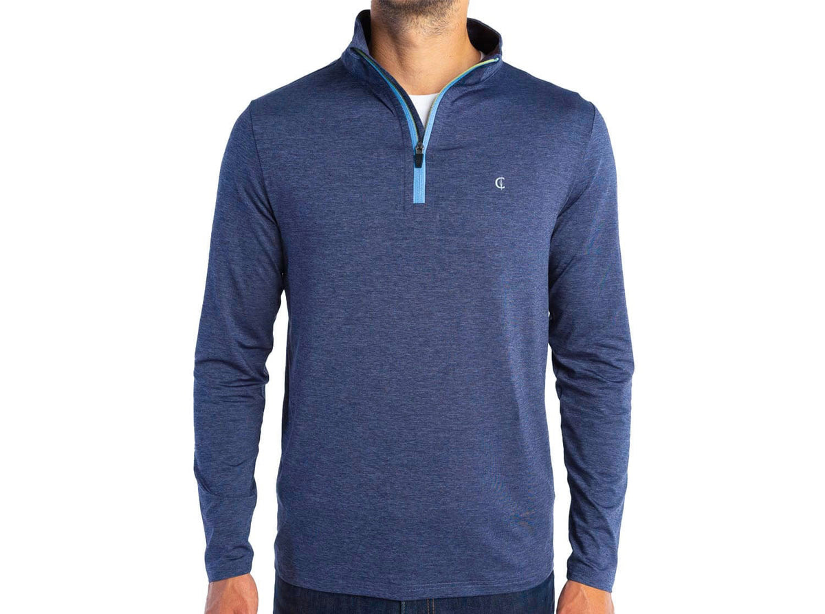 A man wears the CRIQUET FEATHER Performance Knit Quarter Zip Pullover in blue, featuring moisture-wicking fabric, a light blue zipper, and a small chest logo, standing against a plain white background.