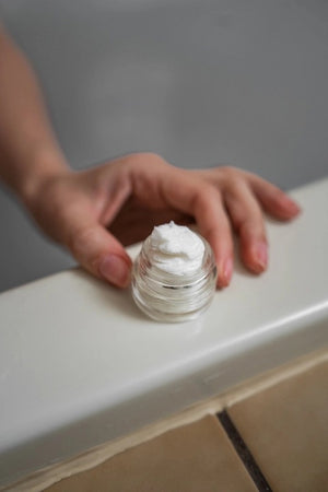 MADISON GREEN’s “REST YOUR EYES IN THE BATH” aromatherapy eye cover packaging is displayed on a white background alongside a small glass jar and two stacked, gift-ready boxes. This minimalist arrangement showcases the soothing MADISON AND GREEN eye covers, crafted with an essential oil blend for ultimate relaxation.