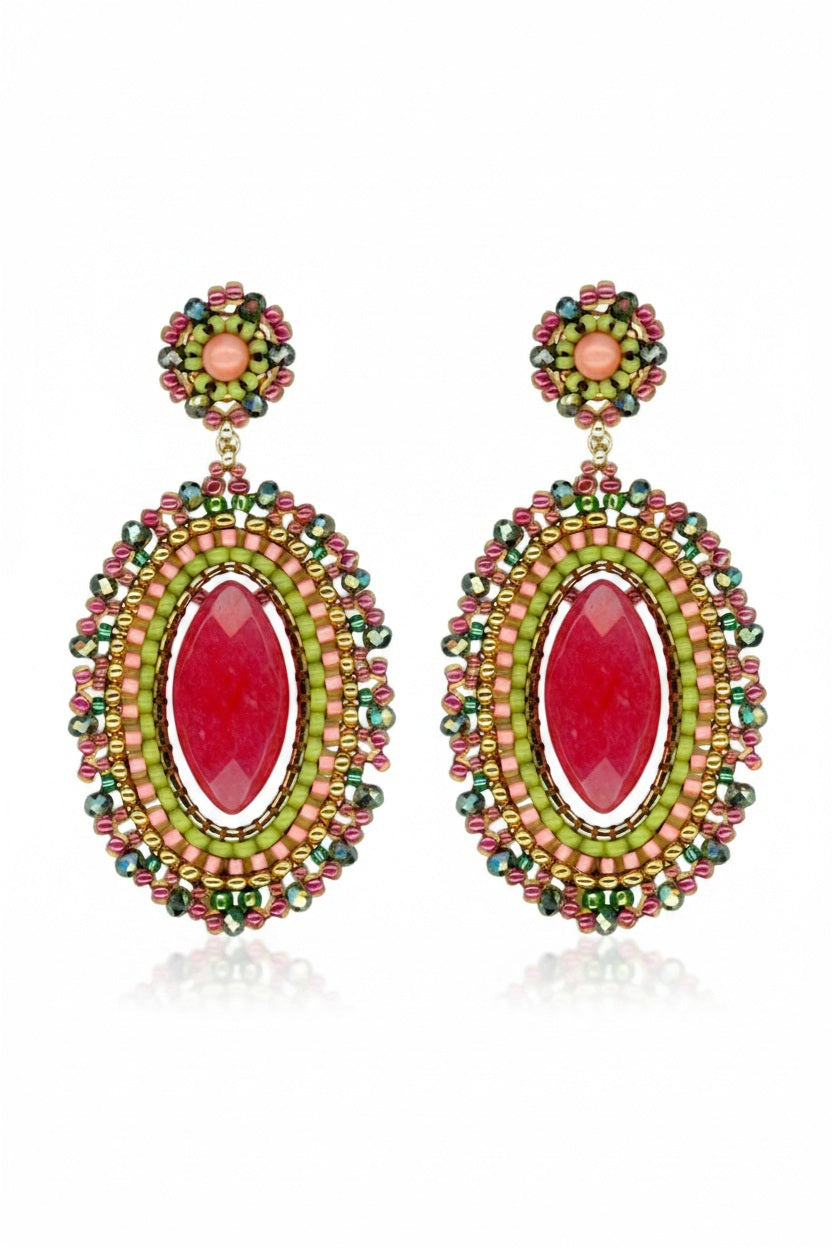 The MIGUEL ASES - CRYSTAL MIYUKI DROP EARRINGS by MIGUEL ASES, INC. are handcrafted, oval-shaped dangle earrings featuring a central red stone and intricate beadwork in red, green, and gold. An ornate design on top complements the vibrant colors of these statement pieces.