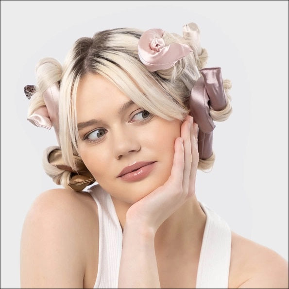 The KITSCH Satin Wrapped Flexi Rods 6 Piece Set by KITSCH features six vegan, satin-wrapped hair rollers in pink, beige, and brown tones. Displayed both inside their packaging and arranged in a fan shape outside, these flexi rods are perfect for creating beautiful heatless curls on curly or wavy hair.
