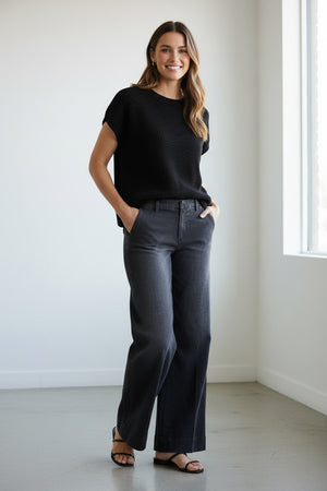 A person stands on a wooden deck, wearing the FRANK & EILEEN West Village NYC Wide Leg Trouser in Italian Dream Light Denim 1981 Wash paired with open-toe sandals. Only the lower half of their body is visible, set against a backdrop of greenery and a white structure, capturing effortless NYC style.