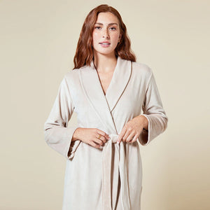 A person wearing a beige SOFTIES - SERENITY WRAP ROBE featuring a wrap silhouette with a tie waist and side pockets.