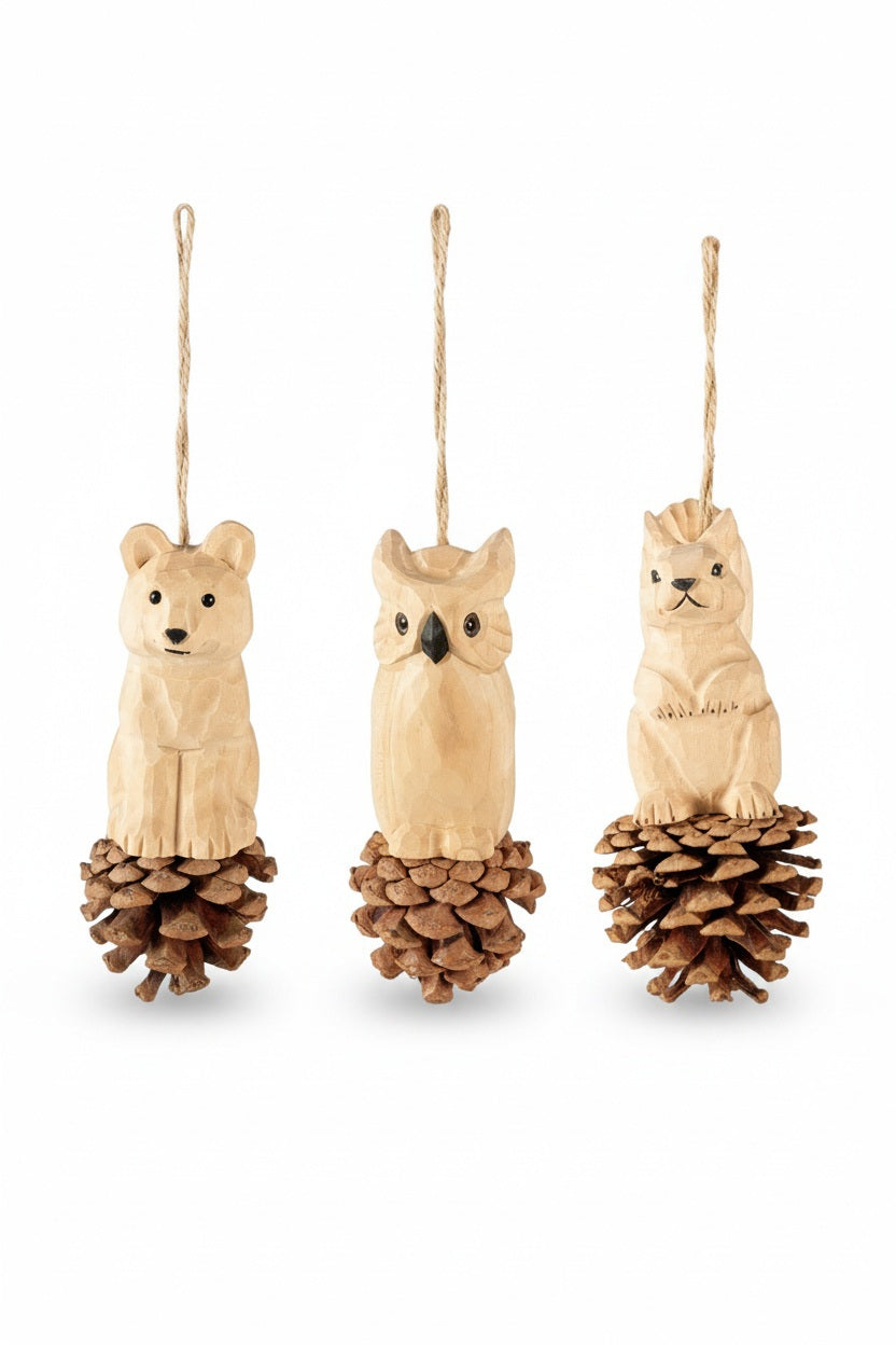 Three HAND CARVED WOOD ANIMAL ON PINECONE ORNAMENT hanging decorations featuring hand-carved basswood animals—a bear, an owl, and a squirrel—each perched on a pinecone base.