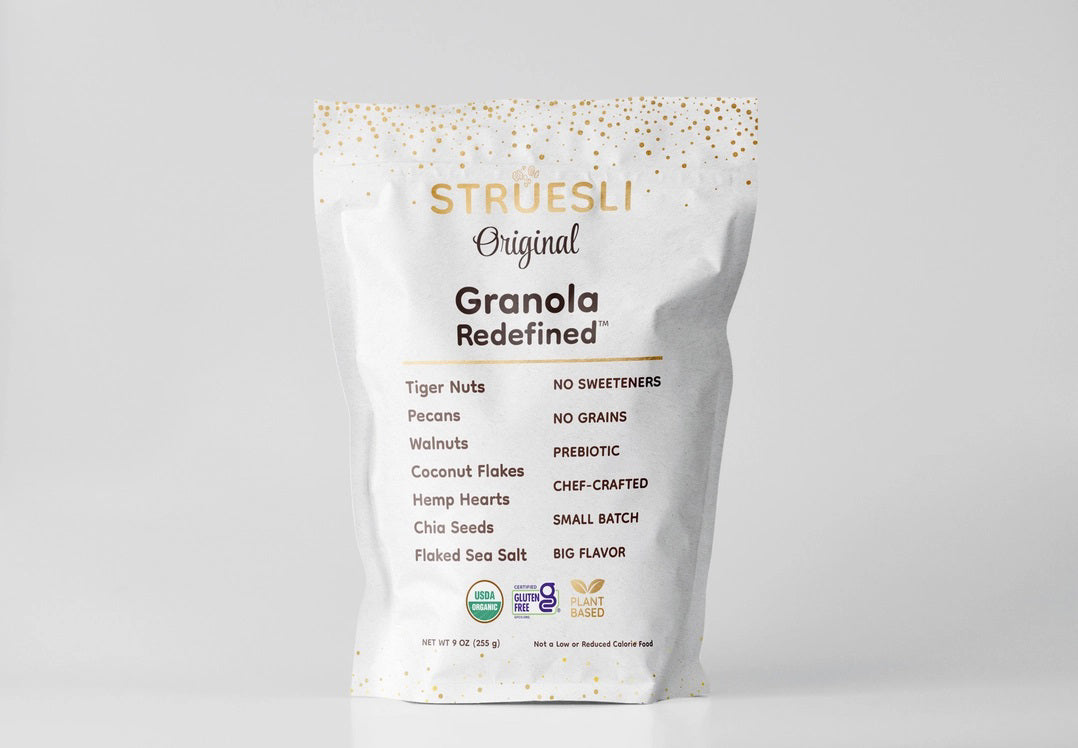 A white bag of STRUESLI - ORIGINAL ORGANIC GRANOLA is displayed against a simple backdrop. The packaging emphasizes that it contains ingredients such as tiger nuts, pecans, walnuts, coconut flakes, among others. Notable features include the absence of sweeteners and grains, along with being rich in plant-based protein for a nutritious boost.