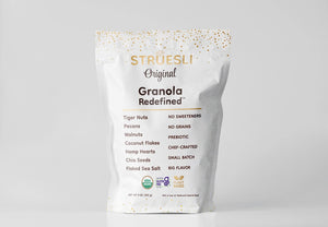 A white bag of STRUESLI - ORIGINAL ORGANIC GRANOLA is displayed against a simple backdrop. The packaging emphasizes that it contains ingredients such as tiger nuts, pecans, walnuts, coconut flakes, among others. Notable features include the absence of sweeteners and grains, along with being rich in plant-based protein for a nutritious boost.