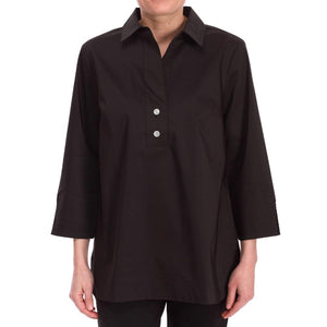 Sporting long hair, the individual is clad in a white HINSON WU - AILEEN TUNIC and black pants. The tunic-length shirt by Hinson Wu features a collar and two buttons near the top. They stand in front of a light gray wall with white molding, with their face not visible in the image.