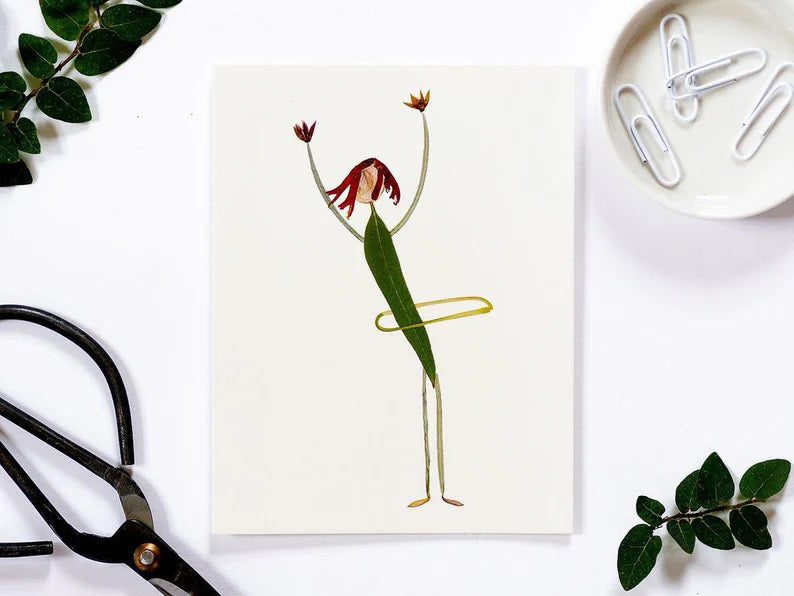 The PETAL PEOPLE PRESS - CARD HULA HOOP features a whimsical illustration of a green, leaf-shaped body person with red hair, hula hooping gracefully. Their stick-like arms and legs are raised in celebration, resembling pressed flower art against a crisp white background.